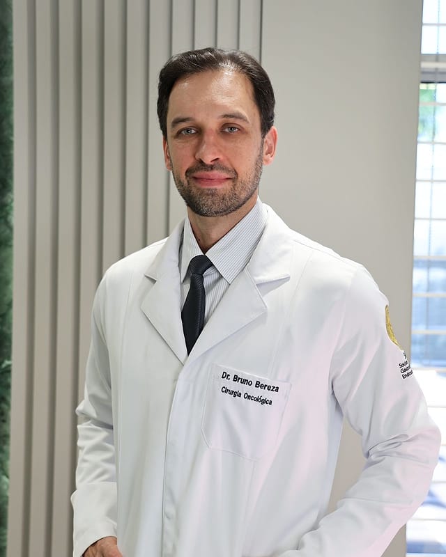 Dr. Bruno Bereza de jaleco, em pé no consultório